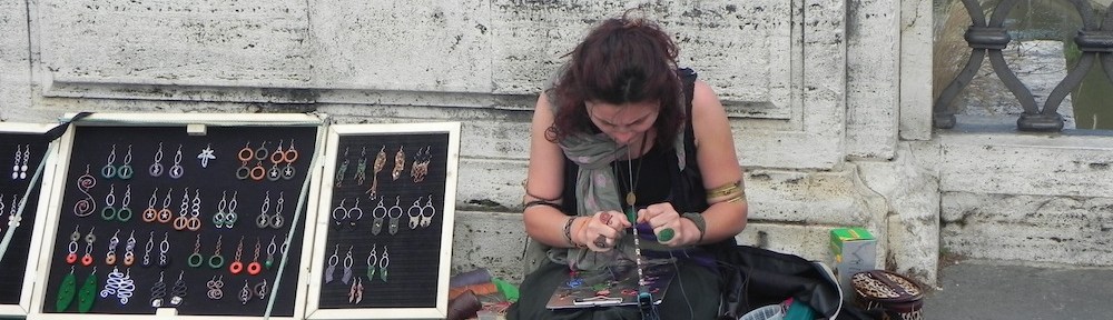 a hippie artists working with threads to create bracelets to sell to tourists at the castel st angelo