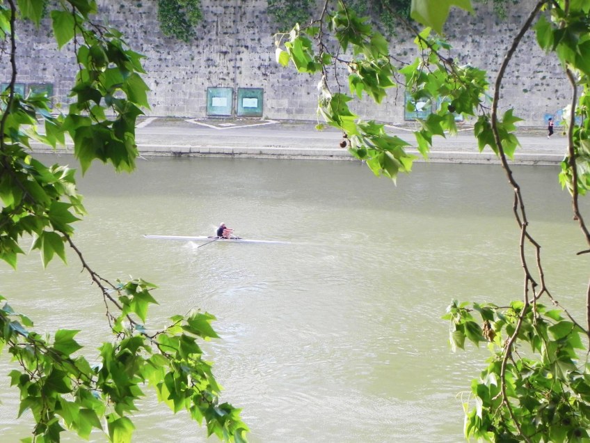a photo of a man canoeing alone in the middle of the river tevere in rome