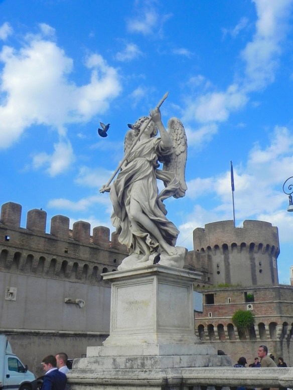 one of the st angelo statue looking as if it is targeting a bird that is truly flying the blue skies