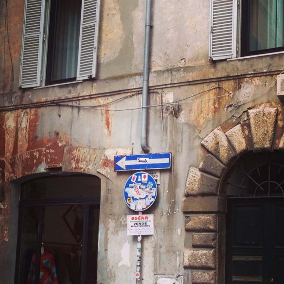 A very humble street sign in rome with an arrow pointing to the left 