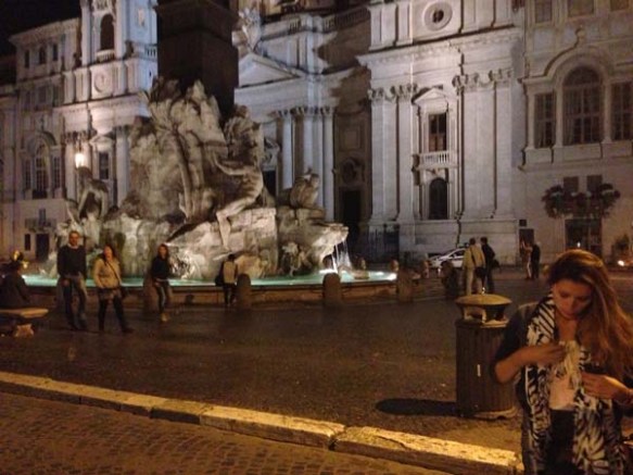 evening photo of razanmasri walking with the fountain of nanona behind 